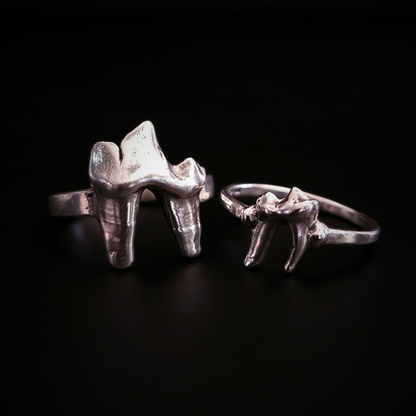 Two gothic style, solid silver rings made using the castings of real fox teeth, sit against a black background, photographed from the front. The sterling silver rings have been oxidised to show the natural wear and texture of the foxes teeh from their lives in the wilderness. Perfect for fans of a witchy and folkloric aesthetics and fans of alternative fashion and oddities.