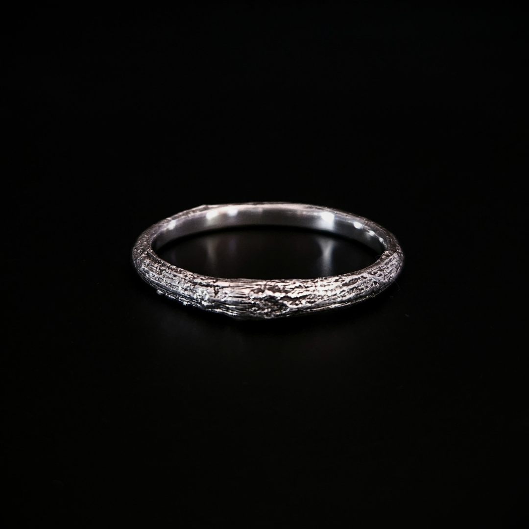 A wood-textured sterling silver band ring shown on a solid black background. The recesses have been oxidised black to reveal the gorgeous oak bark casting on the surface and the inside of the band is completely smooth for comfort.
