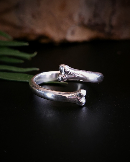 A sterling silver open ring with two bone-ends, photographed on a  black surface with a natural background.
