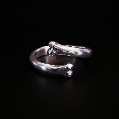 A sterling silver open ring with two bone-ends, photographed on a  black background. The ring reflects a pale glow.