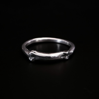 A gothic solid silver ring sits on a black surface. The front side of the ring is a small bone. The details have been oxidised so they show all the natural texture of the bone as it was found in the earth.