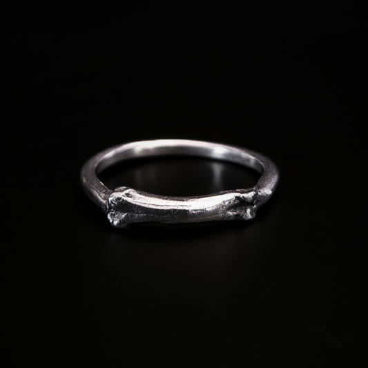 A gothic solid silver ring sits on a black surface. The front side of the ring is a small bone. The details have been oxidised so they show all the natural texture of the bone as it was found in the earth.