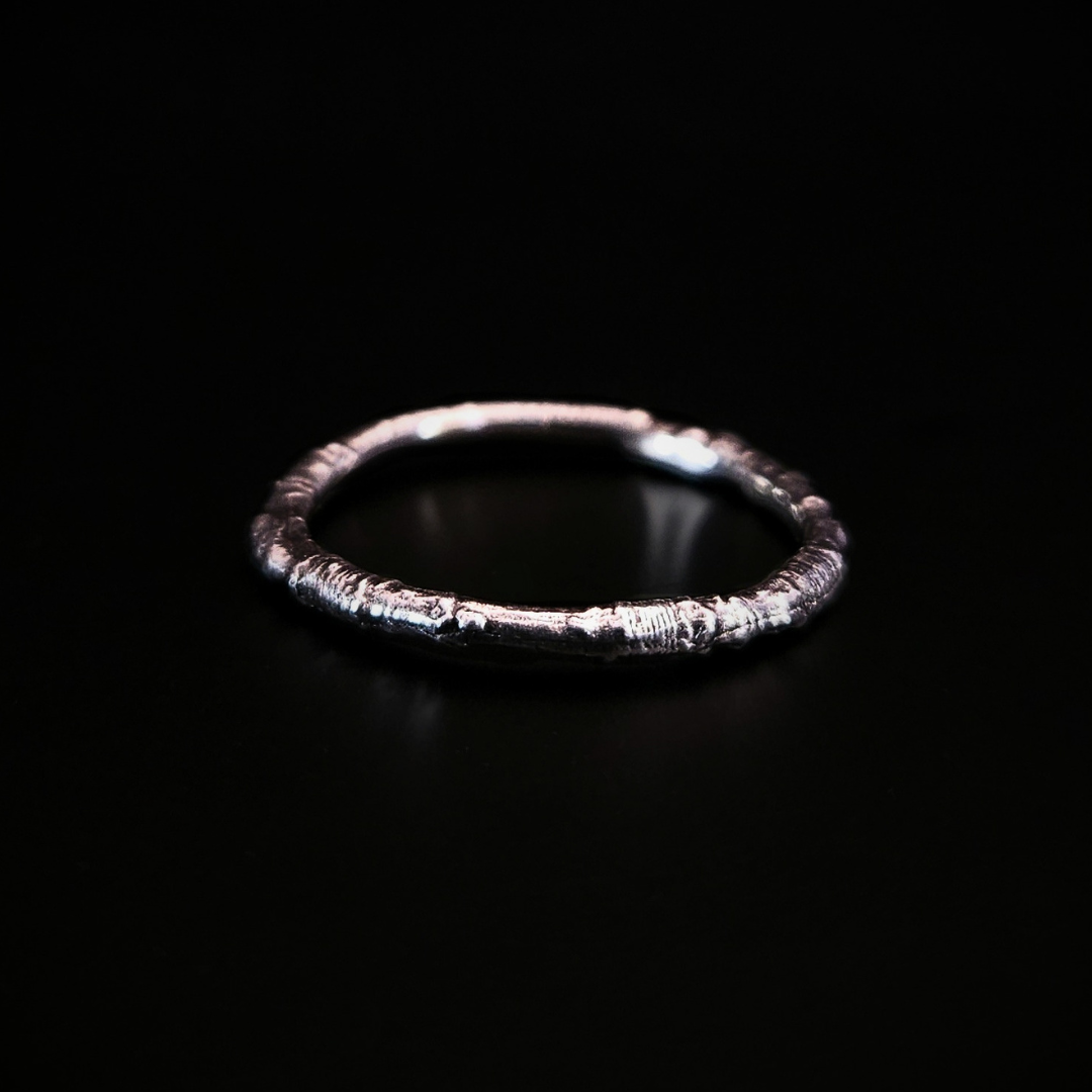 A sterling silver ring made from the casting of a thin twig sits on a black surface. The inside of the ring is nice and smooth for comfort and the light reflects from it in a soft cool glow.