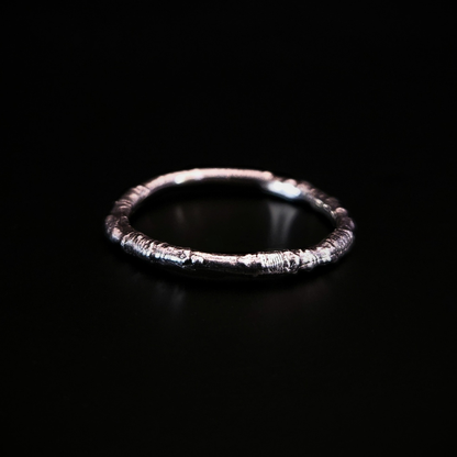 A sterling silver ring made from the casting of a thin twig sits on a black surface. The inside of the ring is nice and smooth for comfort and the light reflects from it in a soft cool glow.
