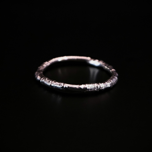 A sterling silver ring made from the casting of a thin twig sits on a black surface. The inside of the ring is nice and smooth for comfort and the light reflects from it in a soft cool glow.