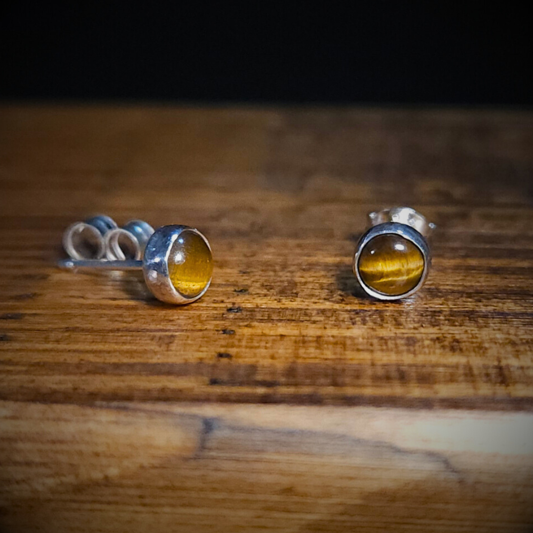 A pair of round sterling silver & tiger's eye gemstone stud earrings on a wooden surface