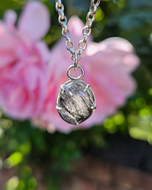 Sterling silver and tourmalinated quartz necklace with a pendant in front of pink flowers