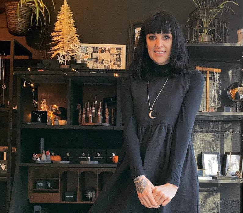 Woman in a black dress standing in a witchy room wearing a large crescent moon pendant in solid sterling silver.
