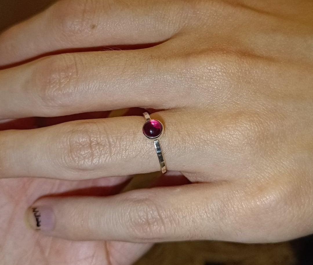 Hand wearing a dainty sterling silver ring with a blood red garnet