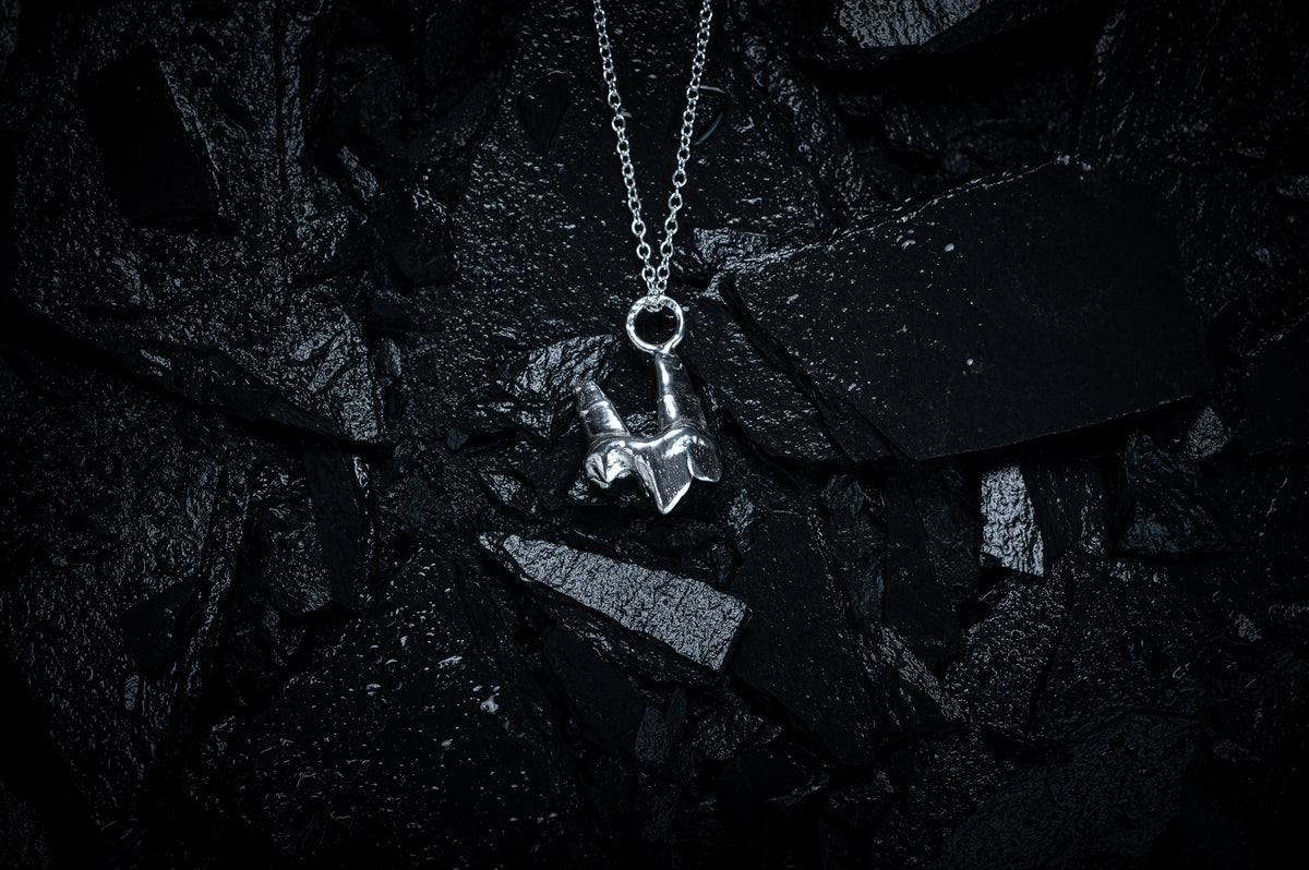 A silver necklace made from the casting of a baby fox tooth sits on a background of wet, black slate. The photograph is taken from the top down. This is a stunning taxidermy style pendant for fans of alternative jewellery, folklore and witchy, gothic aesthetics.