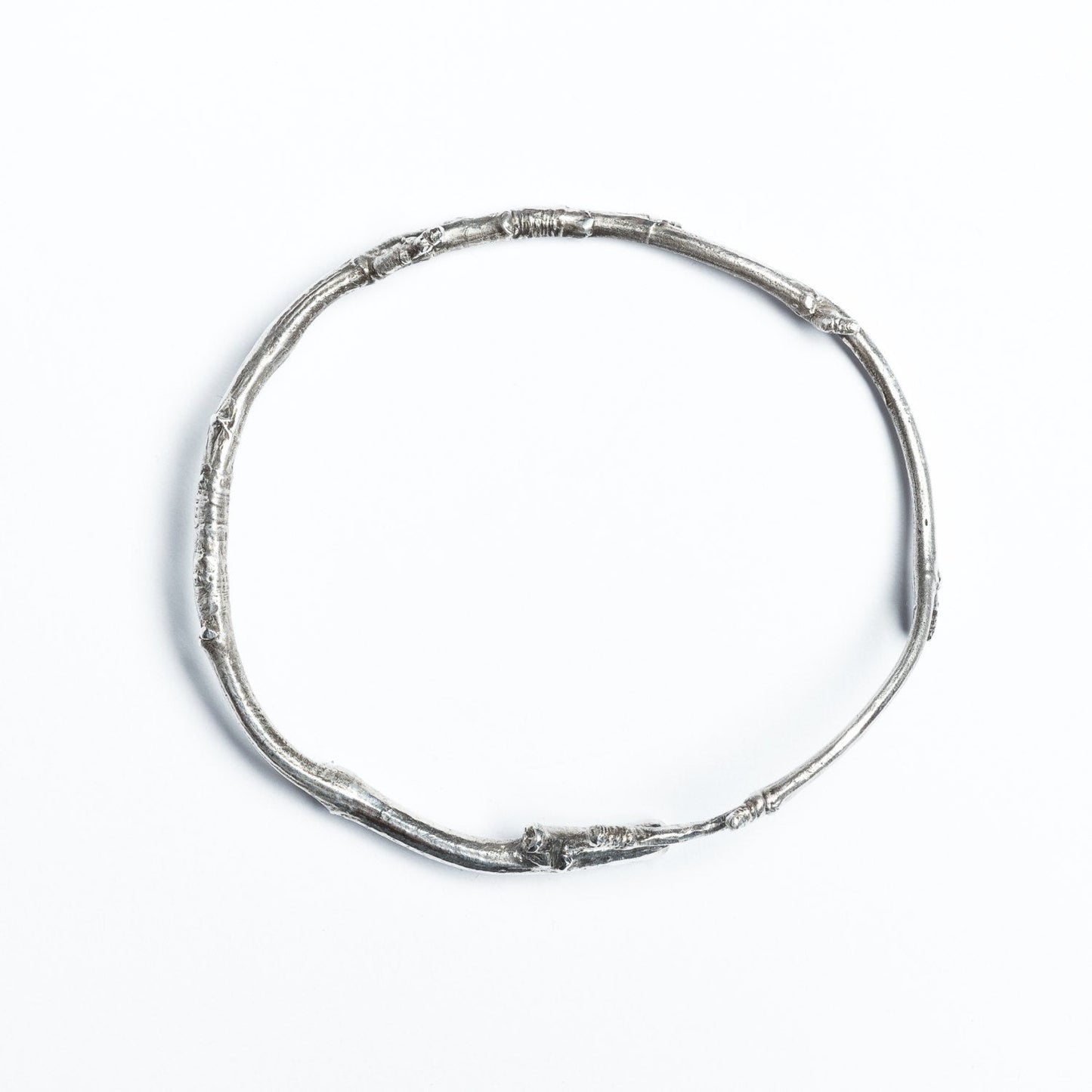 A solid silver twig, wrapped into a bracelet, is photographed from above on a white background