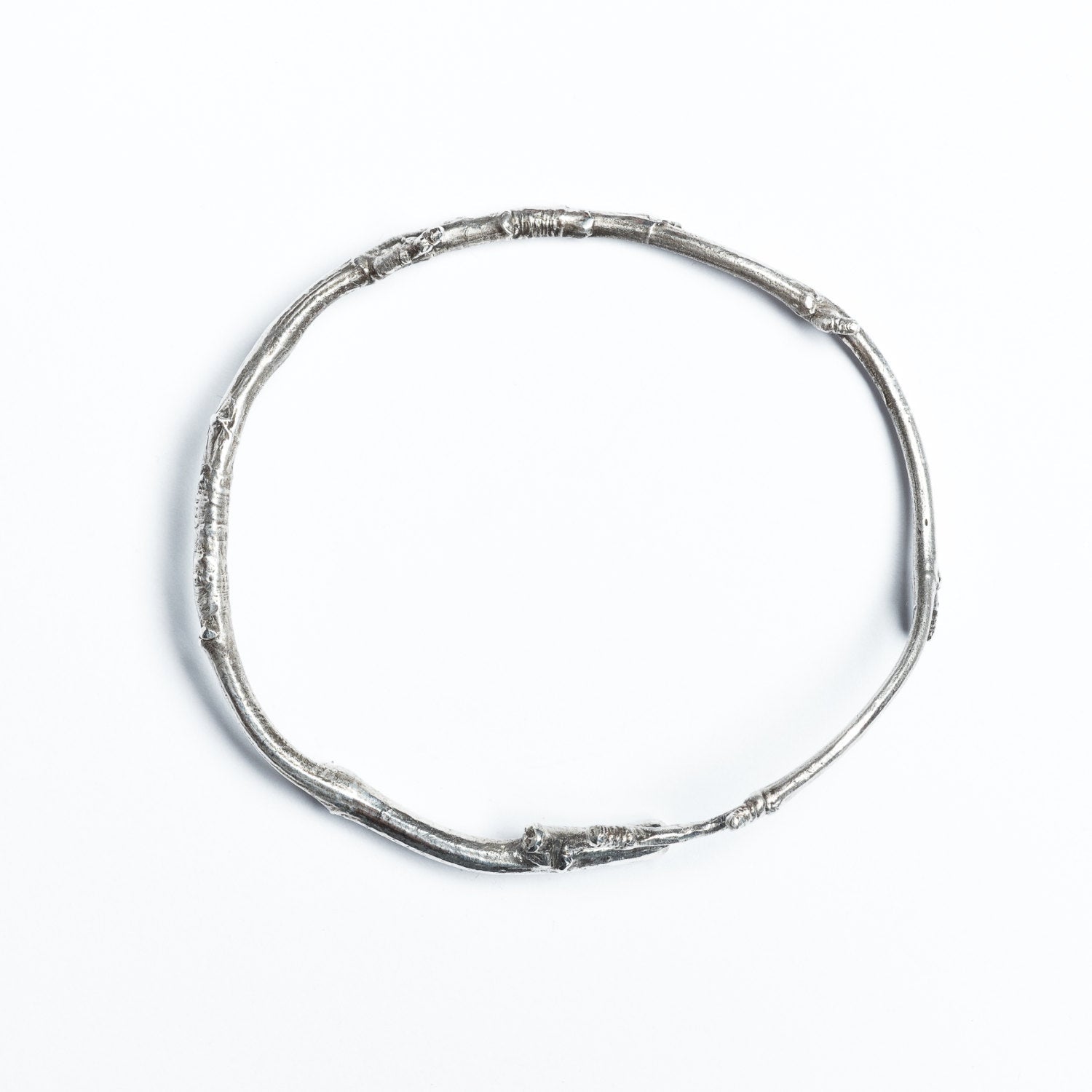 A solid silver twig, wrapped into a bracelet, is photographed from above on a white background