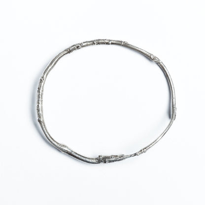 A solid silver twig, wrapped into a bracelet, is photographed from above on a white background